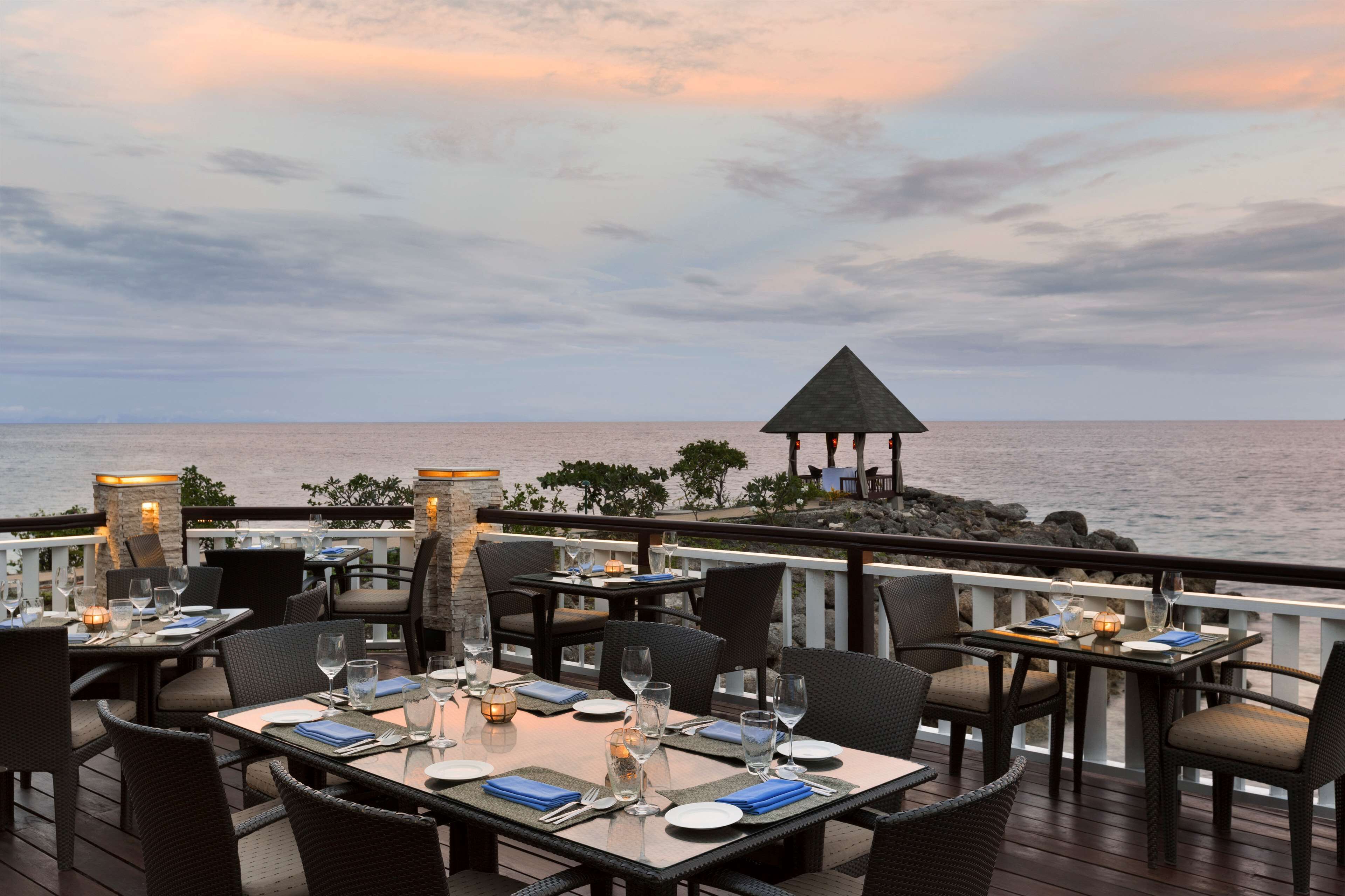 An outdoor dining area with tables and chairs, overlooking the sea.