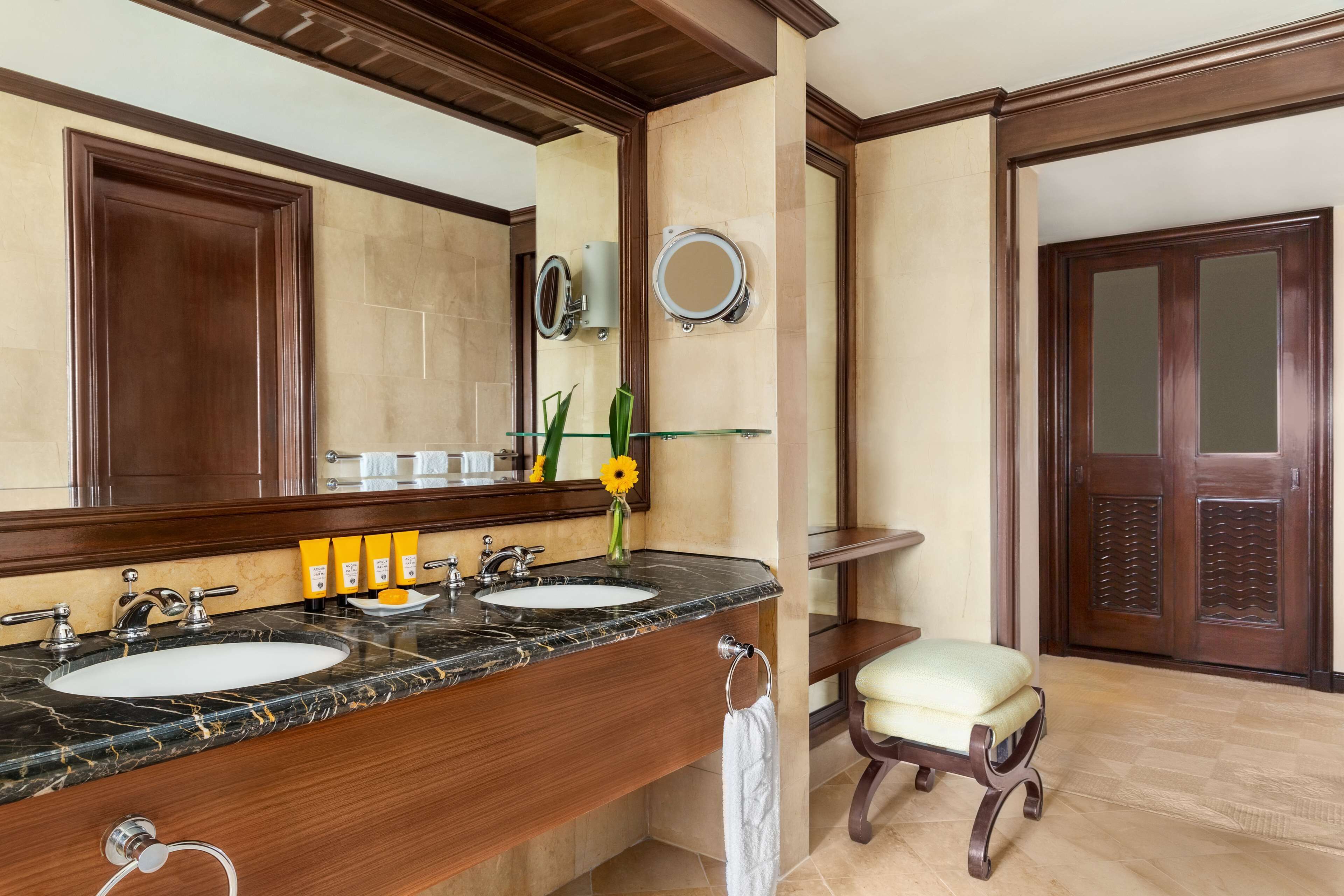 Un baño con dos lavamanos, un espejo grande, un perchero para toallas y un banco de madera.