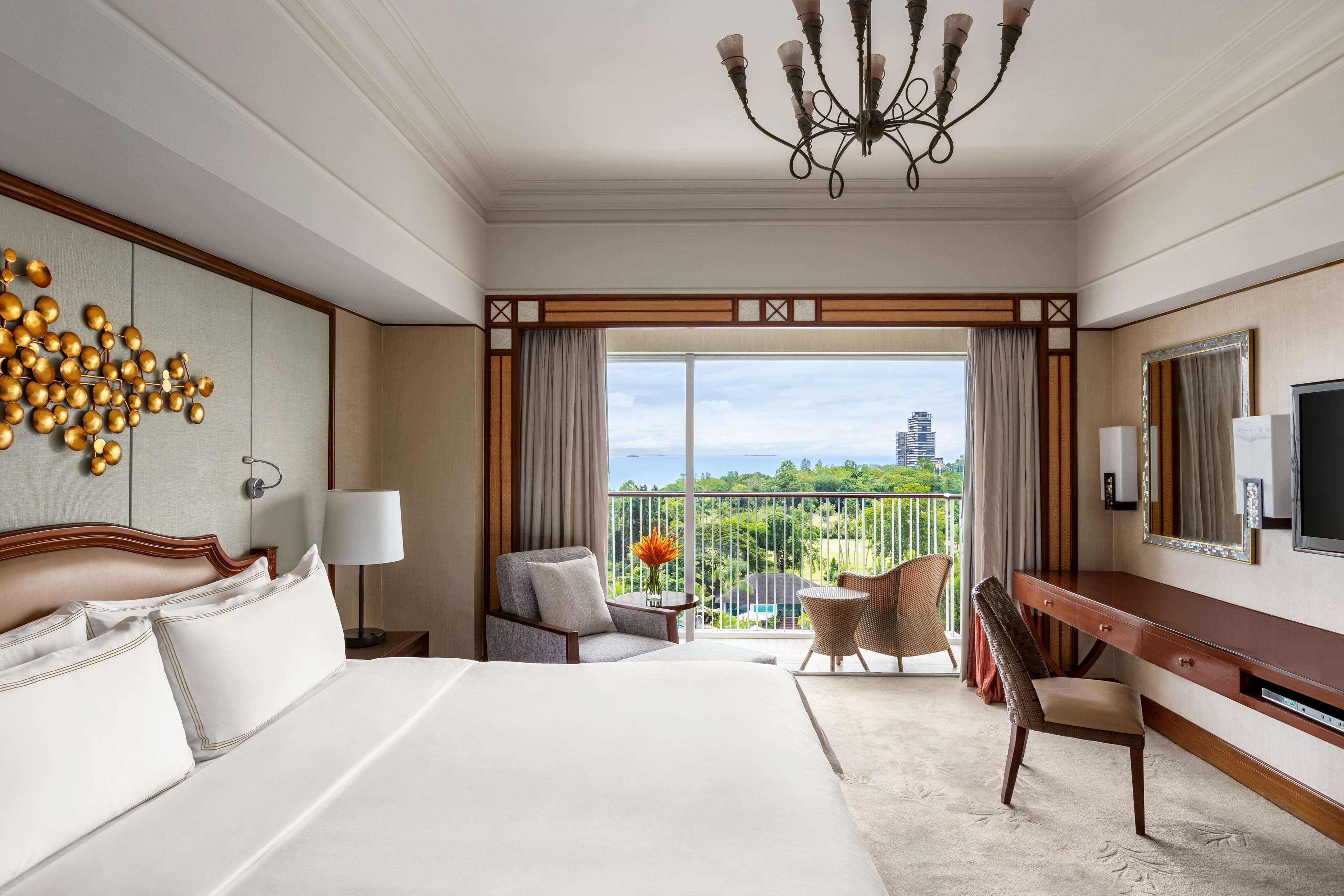 A hotel room with a large bed, a desk, a chair, a TV, and a balcony with a view.
