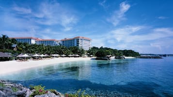 Un resort con playa, aguas azules cristalinas y un edificio grande con varios balcones.