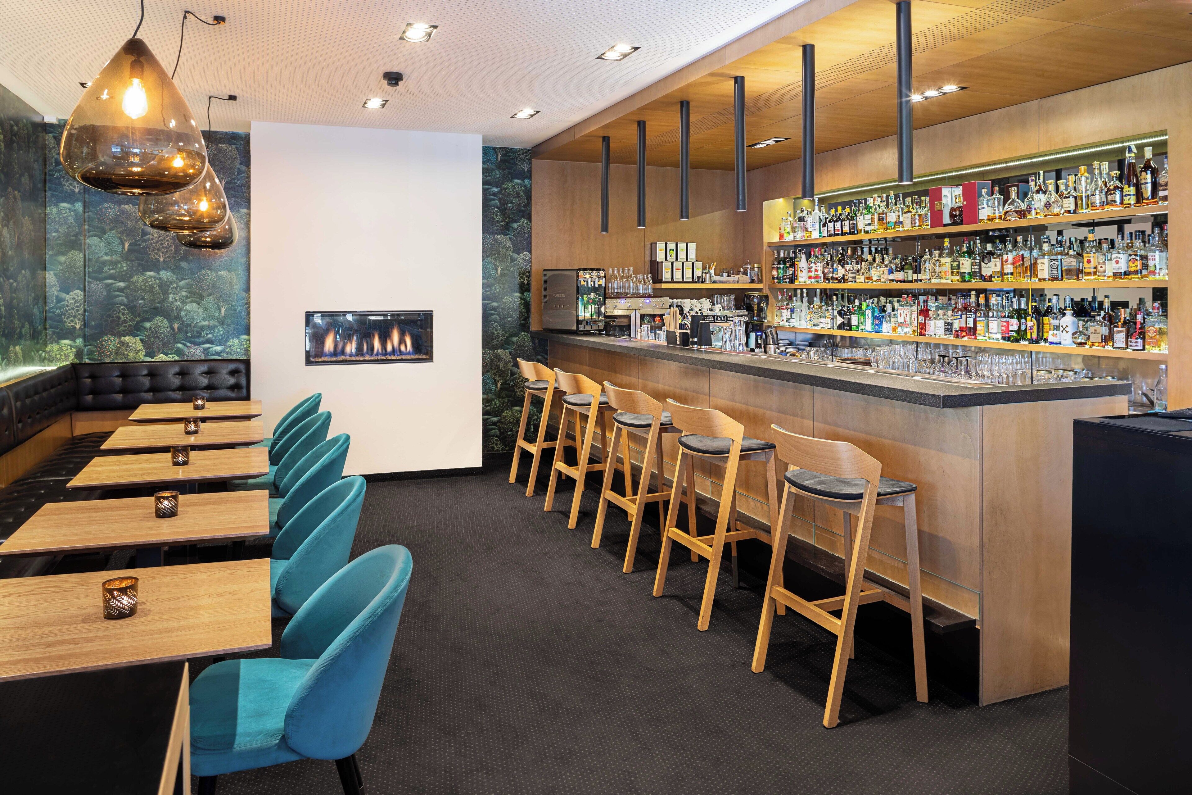 A bar area with multiple seating options, including bar stools and tables, and a variety of liquor bottles on shelves.