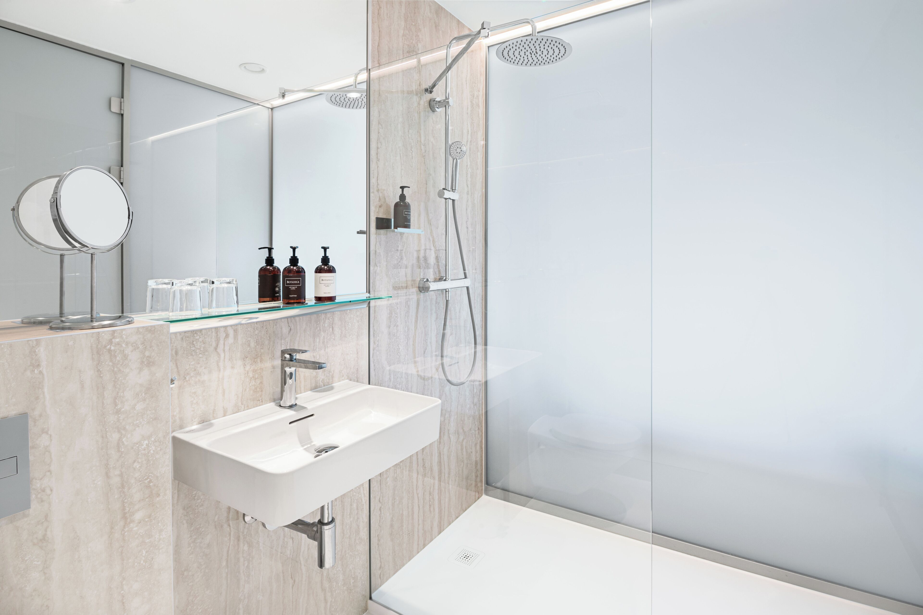 A modern bathroom with a glass shower enclosure, a white sink, and a mirror.