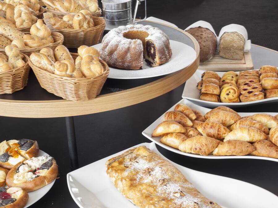 Una mesa de buffet con diversas opciones de panadería, incluyendo pan, bollos y pasteles.