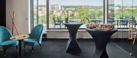 A modern room with large windows, a view of a cityscape, a table with food, and a blue chair.
