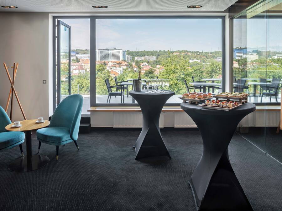 A modern room with large windows, a view of a cityscape, a table with food, and a blue chair.