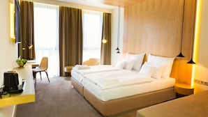 Hotelkamer met een groot bed, nachtkastjes, een bureau met stoel en uitzicht op het landschap door grote ramen.