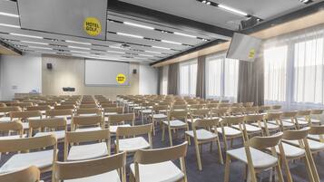 A conference room with rows of chairs, a projector screen, and a "Hotel Golf" sign.
