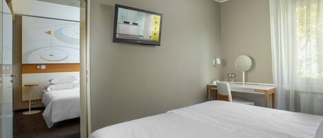 Habitación de hotel con cama, escritorio, silla, televisor montado en la pared y ventana con cortinas.