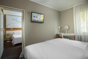 Camera d'albergo con un letto, una scrivania, una sedia, una televisione fissata al muro e una finestra con tende.