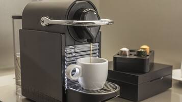 Une machine à café Nespresso avec une tasse placée sous le bec verseur, un verre d’eau et une petite boîte contenant une bougie.