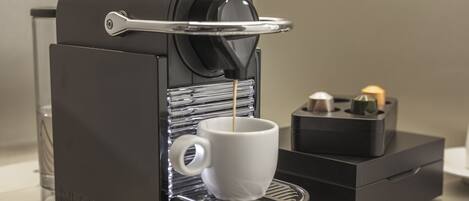 Una máquina de café Nespresso con una taza debajo del caño, un vaso de agua y una pequeña caja con una vela.