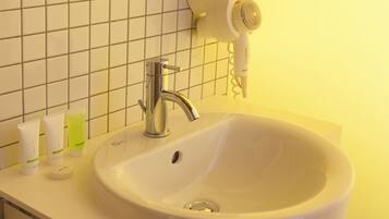 A bathroom sink with a chrome faucet, a hairdryer, and toiletries on the counter.