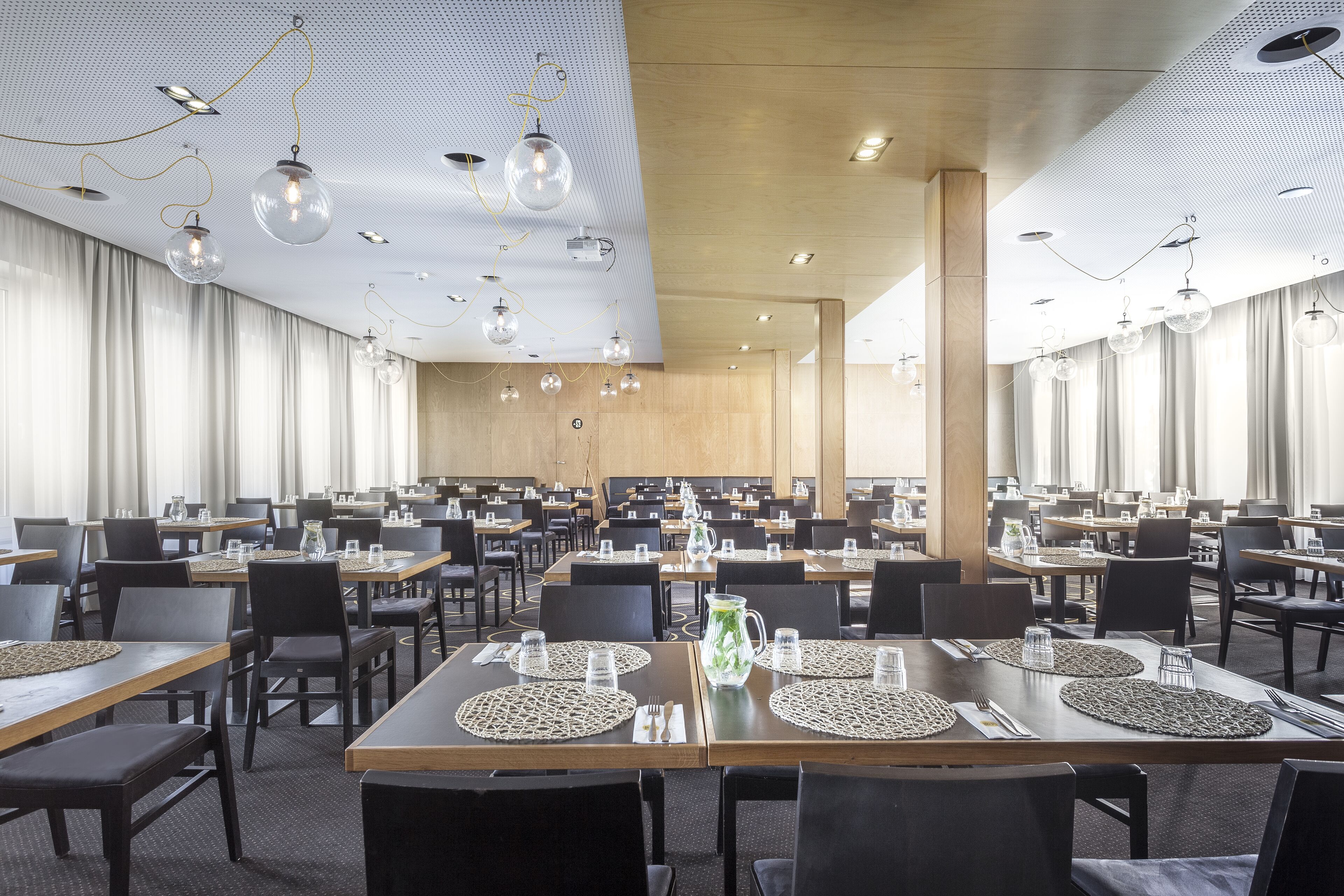 Un comedor amplio con varias mesas, sillas e iluminación colgante.