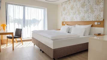 Quarto de hotel com uma cama grande, uma escrivaninha com cadeira e vista para o exterior pela janela.