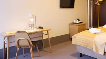 Una habitación de hotel con escritorio, silla, cama, televisor y un mueble pequeño con cafetera.
