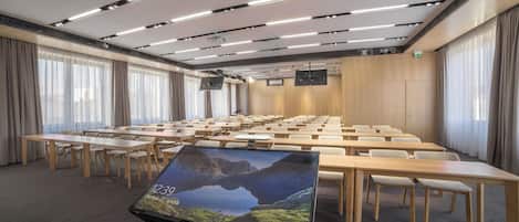 Una sala conferenze con un grande schermo, diversi tavoli e sedie disposte per riunioni.