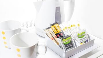 Uma cafeteira branca, duas chávenas brancas com pontos amarelos e um tabuleiro branco com saquetas de chá Pickwick.