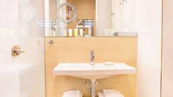 Un baño moderno con cabina de ducha de vidrio, un lavamanos blanco con grifo dorado y un mueble de tocador de madera.