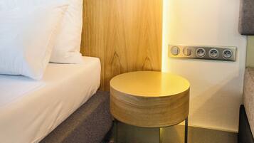 A neatly arranged hotel room with a wooden headboard, a round wooden side table, and a bed with white bedding.