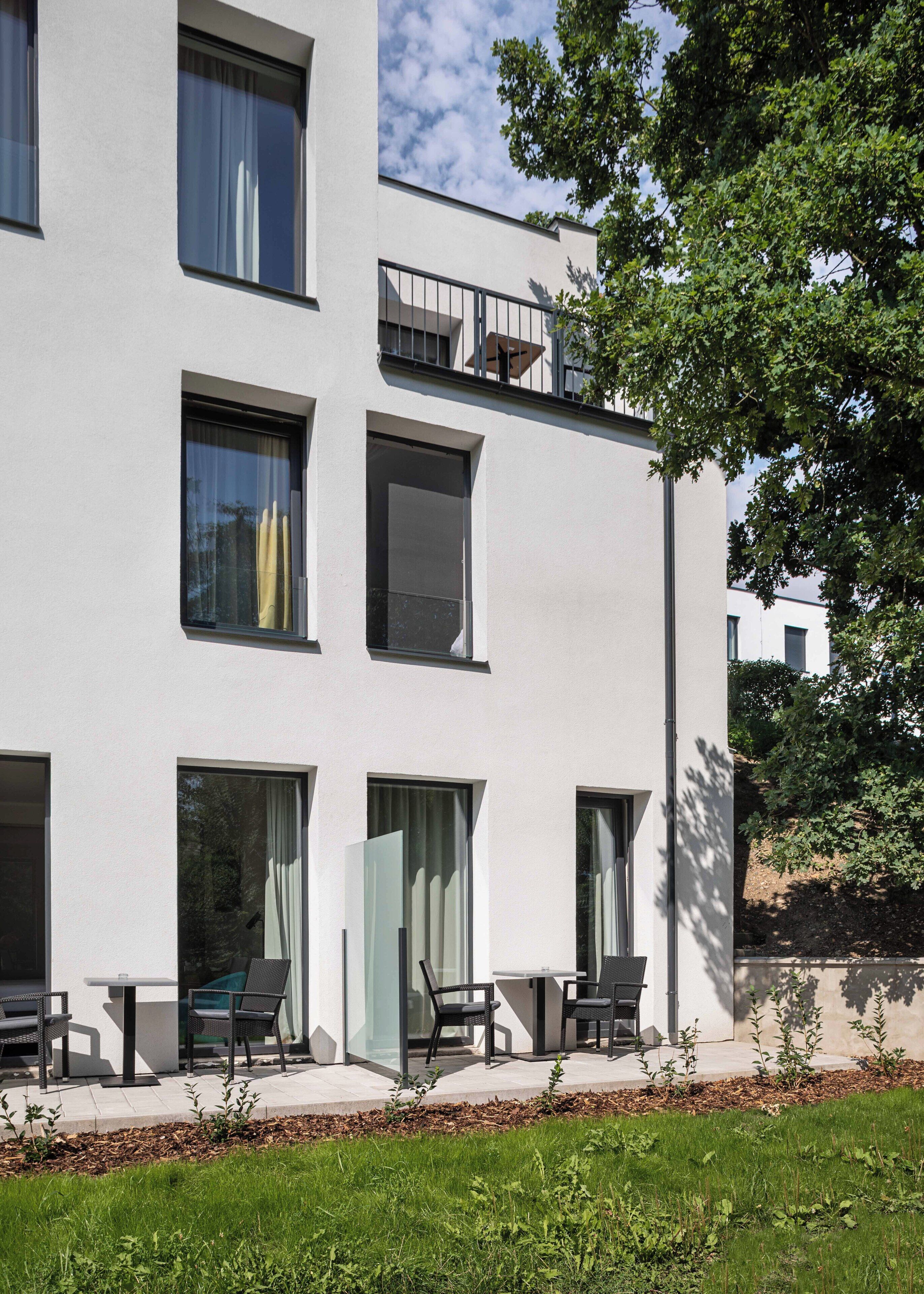 Un edificio moderno con múltiples ventanas, un balcón y mobiliario exterior.