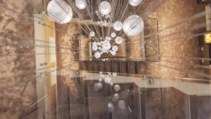 Een modern interieur met een glazen trap en een kroonluchter met meerdere bolvormige lampen.