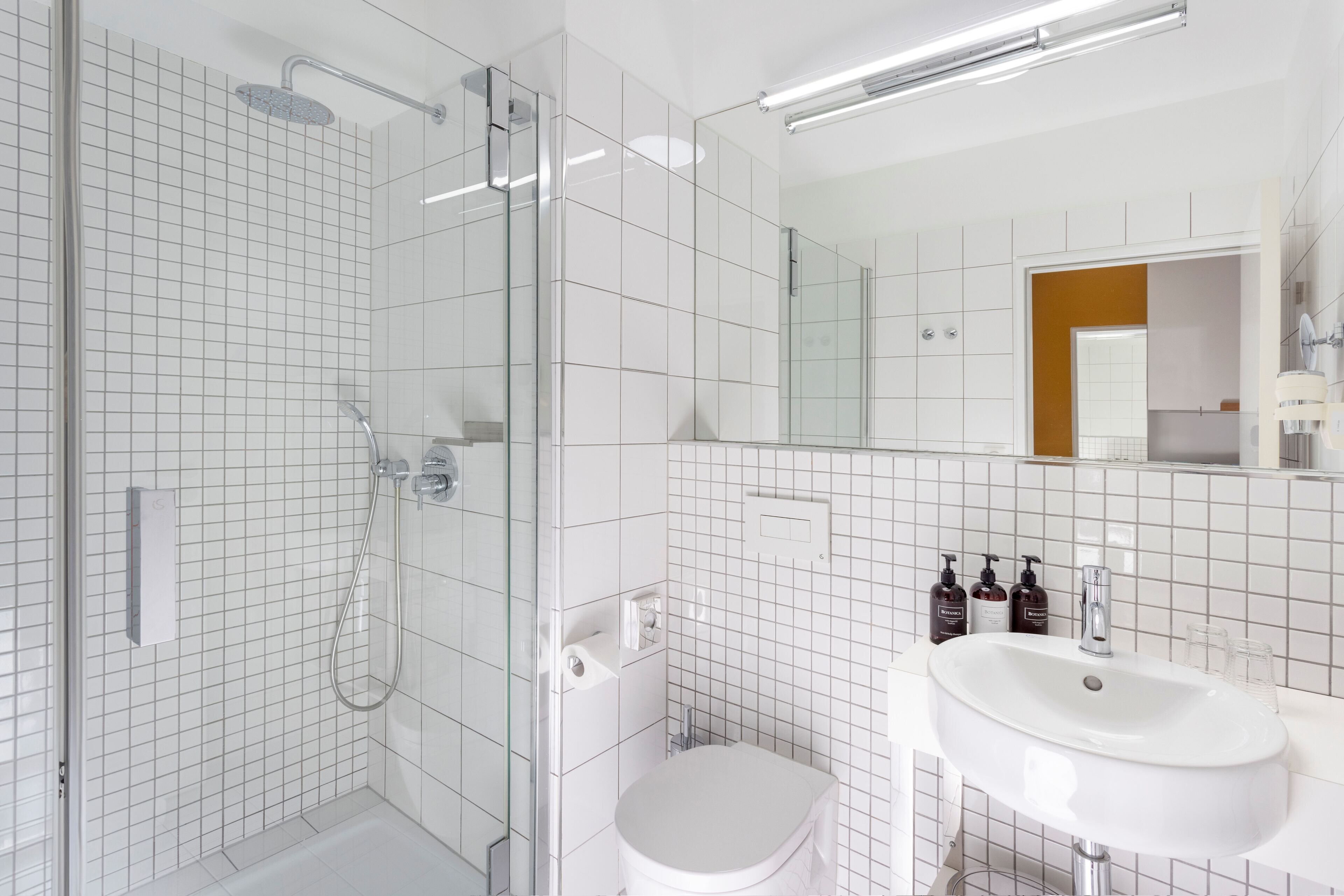 A modern bathroom with a glass-enclosed shower, a white toilet, and a sink with a mirror above it.