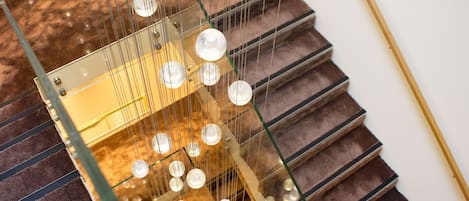 Una escalera con barandilla de vidrio y luces esféricas colgantes.