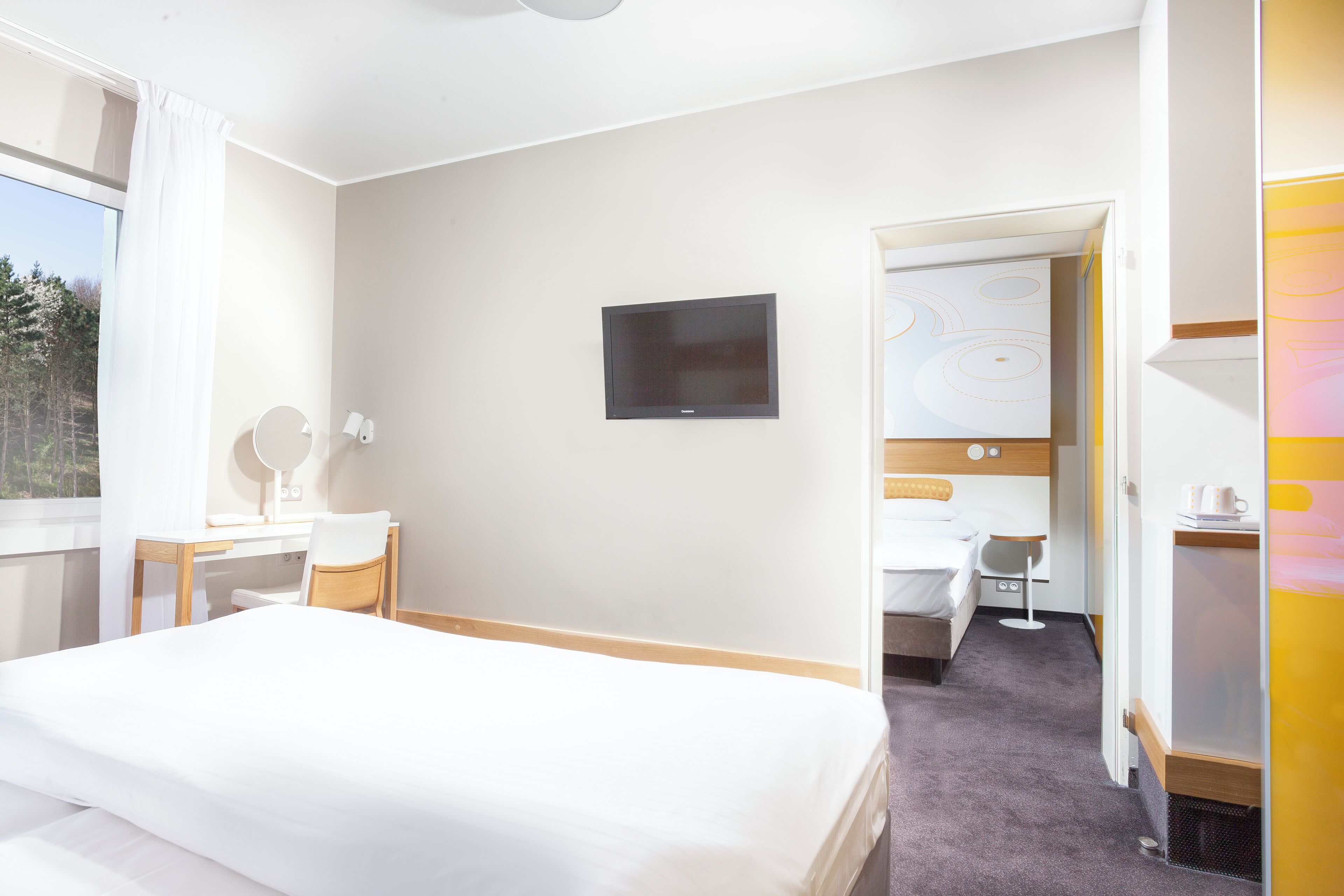 A hotel room with a bed, desk, chair, and a TV on the wall.