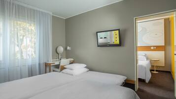 Habitación de hotel con una cama grande, un escritorio con silla, una mesita de noche, un televisor y una puerta que da a otra habitación.