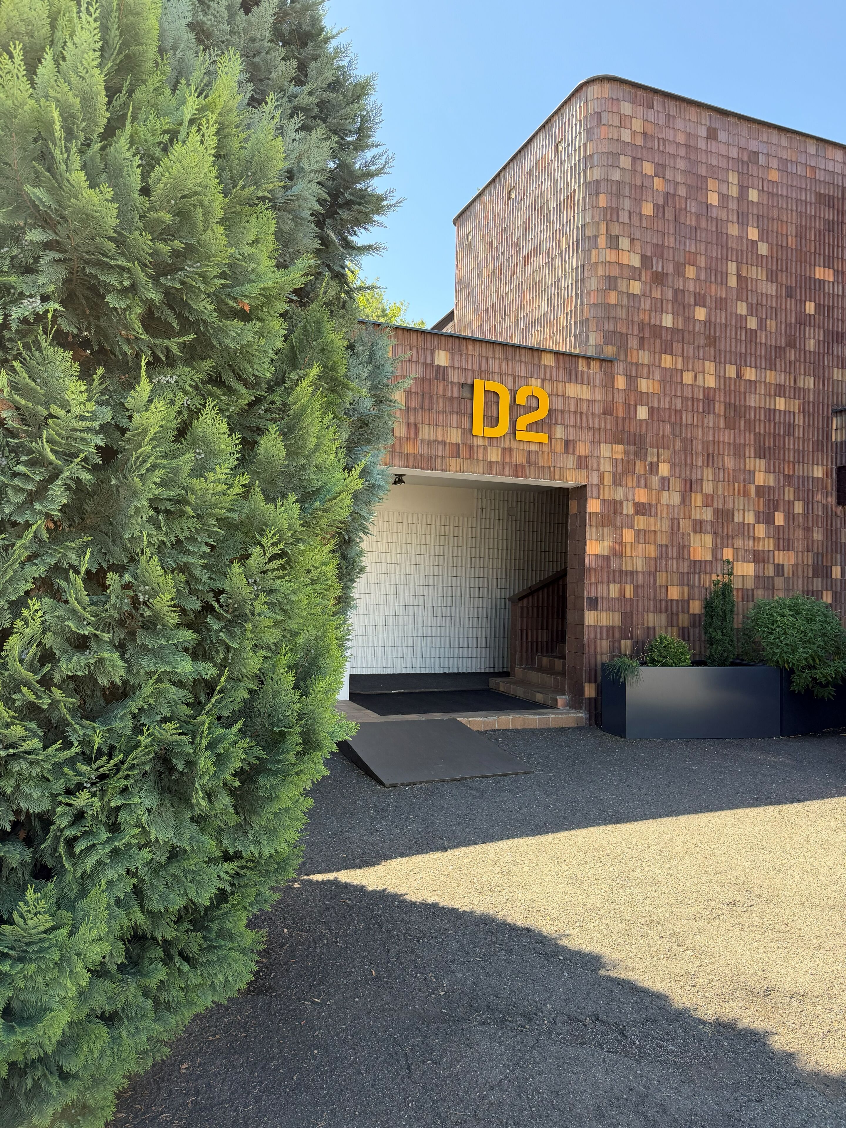 A modern building with a 'D2' sign, a covered entrance, and a gravel driveway.