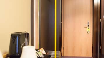 A hotel room with a wooden desk, a coffee machine, a coat rack, and a door with a lock.