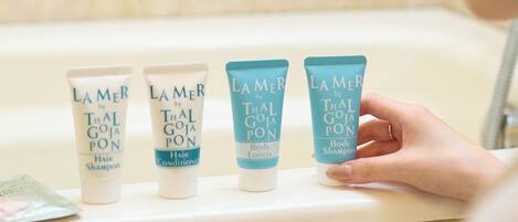 A bathroom with four Lamer by Thal Goja Pon hair and body care products on a shelf.