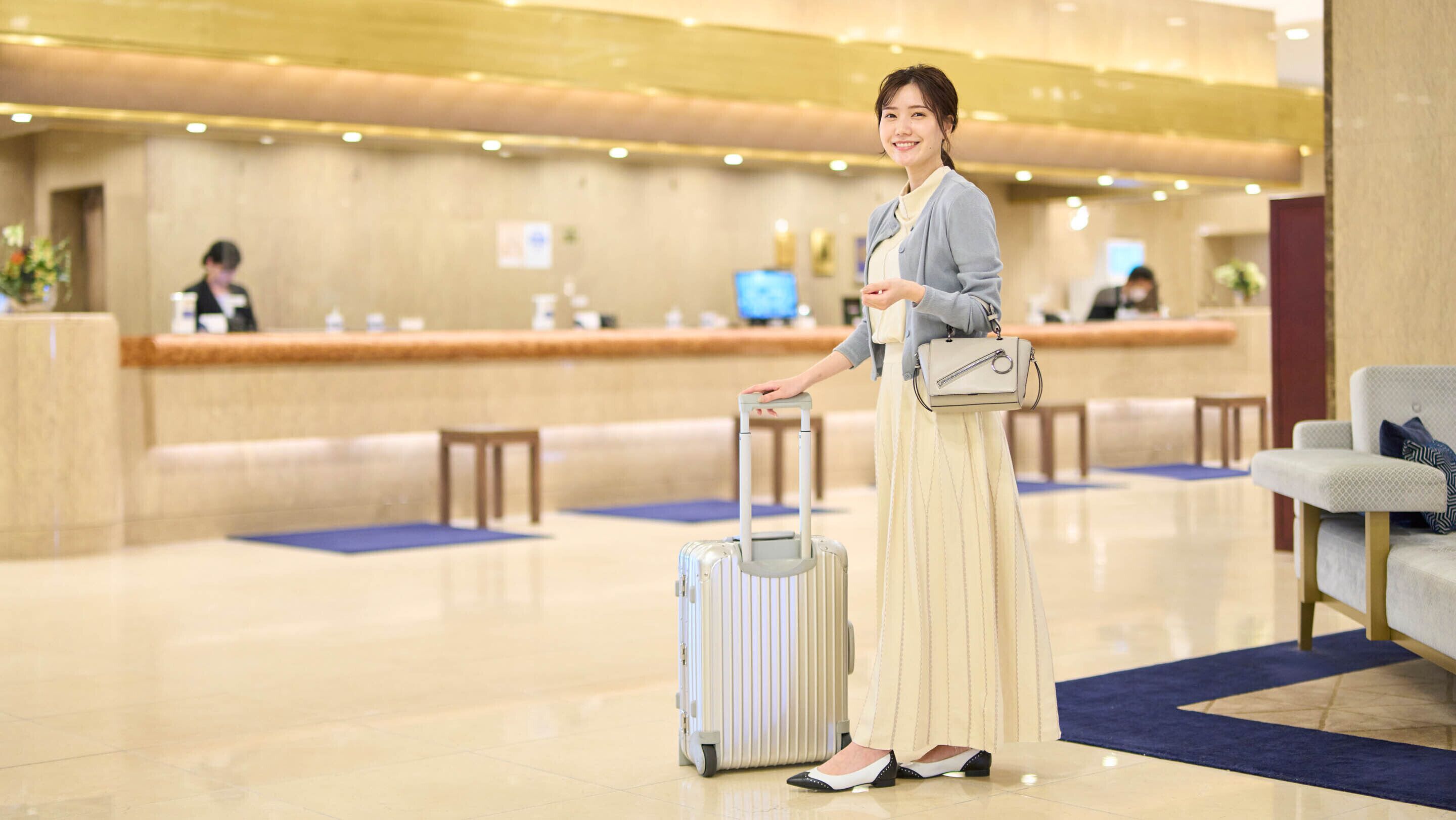 A person with a suitcase in a hotel lobby with a reception desk and seating area.