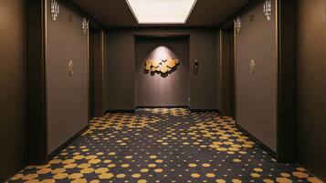 A hallway with a patterned floor, a wall-mounted light fixture, and a door with a number.