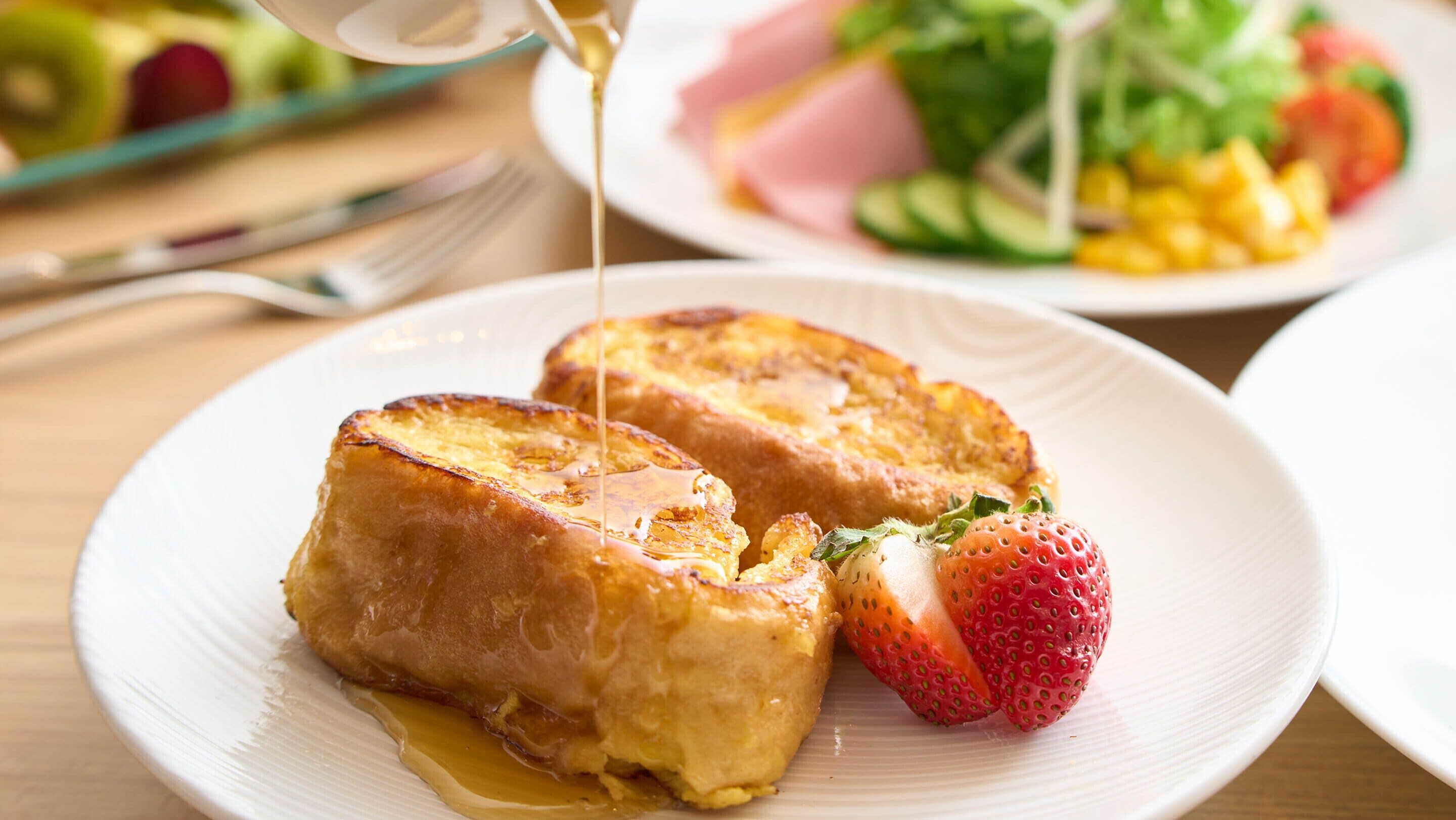 A plate of French toast with syrup and strawberries.
