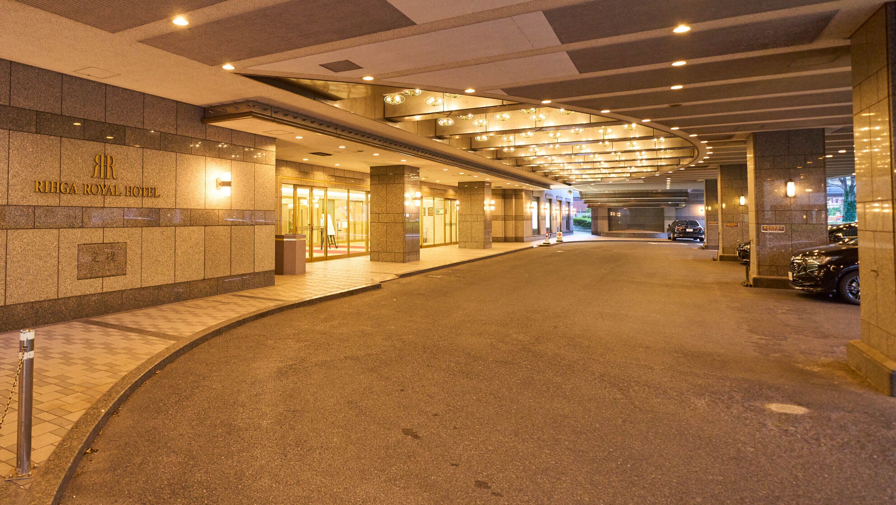 The entrance of the RIHGA ROYAL HOTEL with a covered walkway and a parking area.