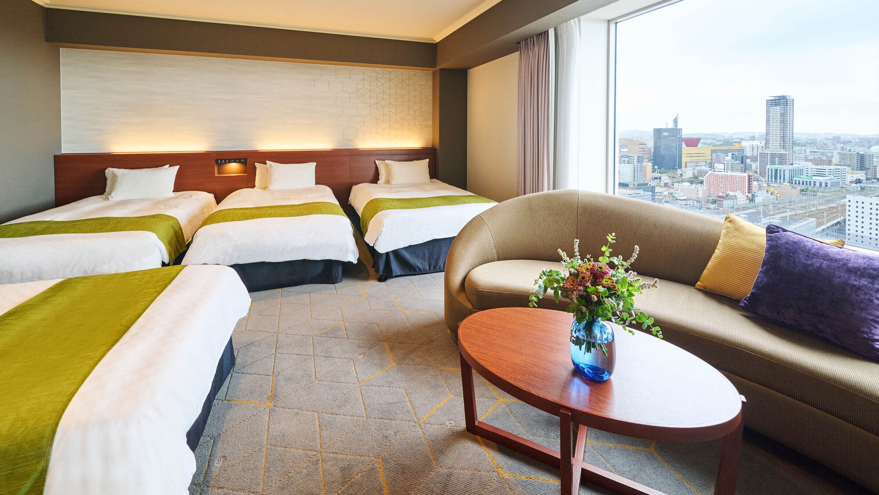 A hotel room with two beds, a sofa, a coffee table, and a city view.
