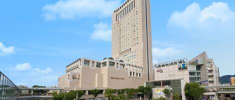 A modern hotel with a tall central tower, a covered walkway, and a parking area.