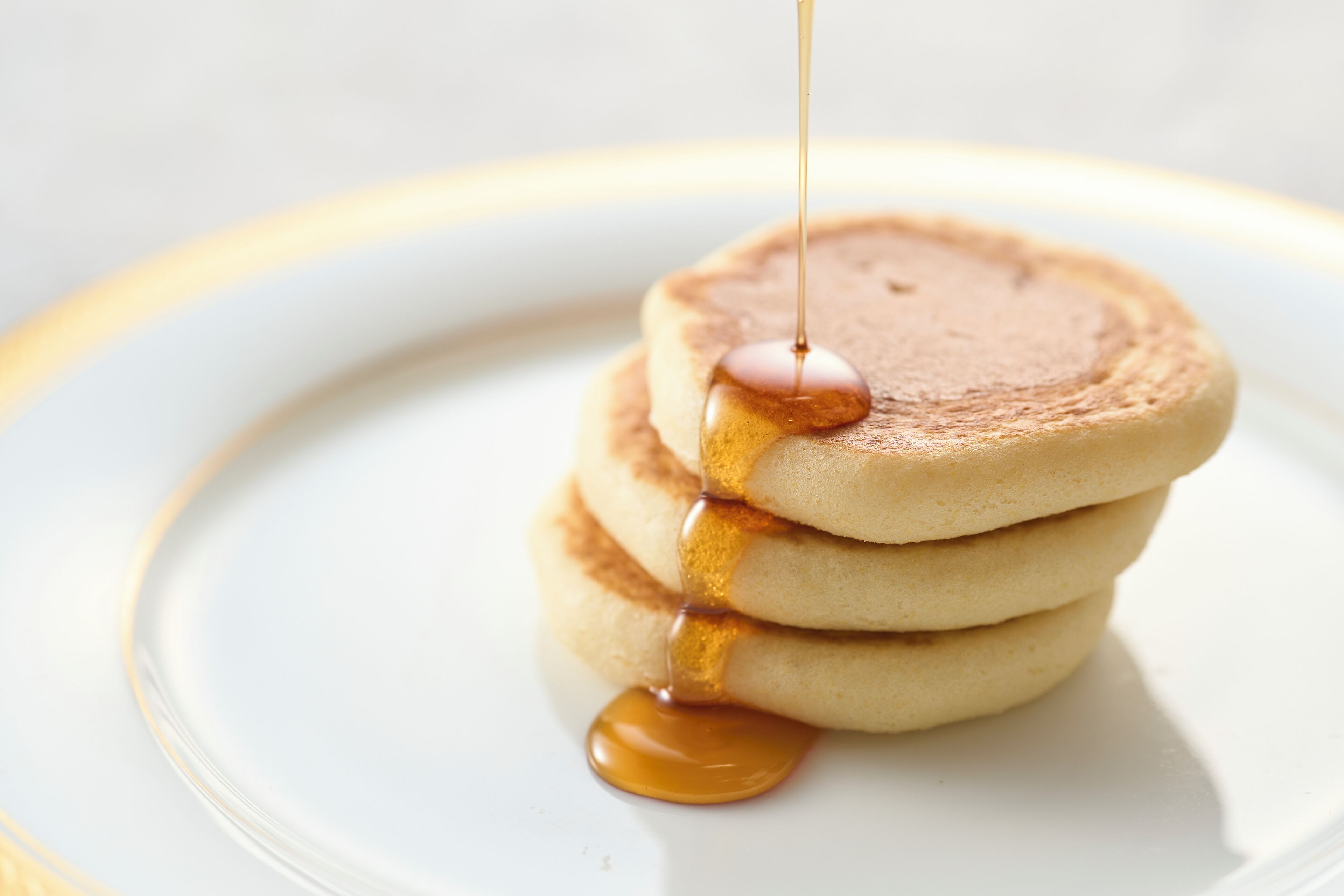 A stack of pancakes with syrup being poured over them.