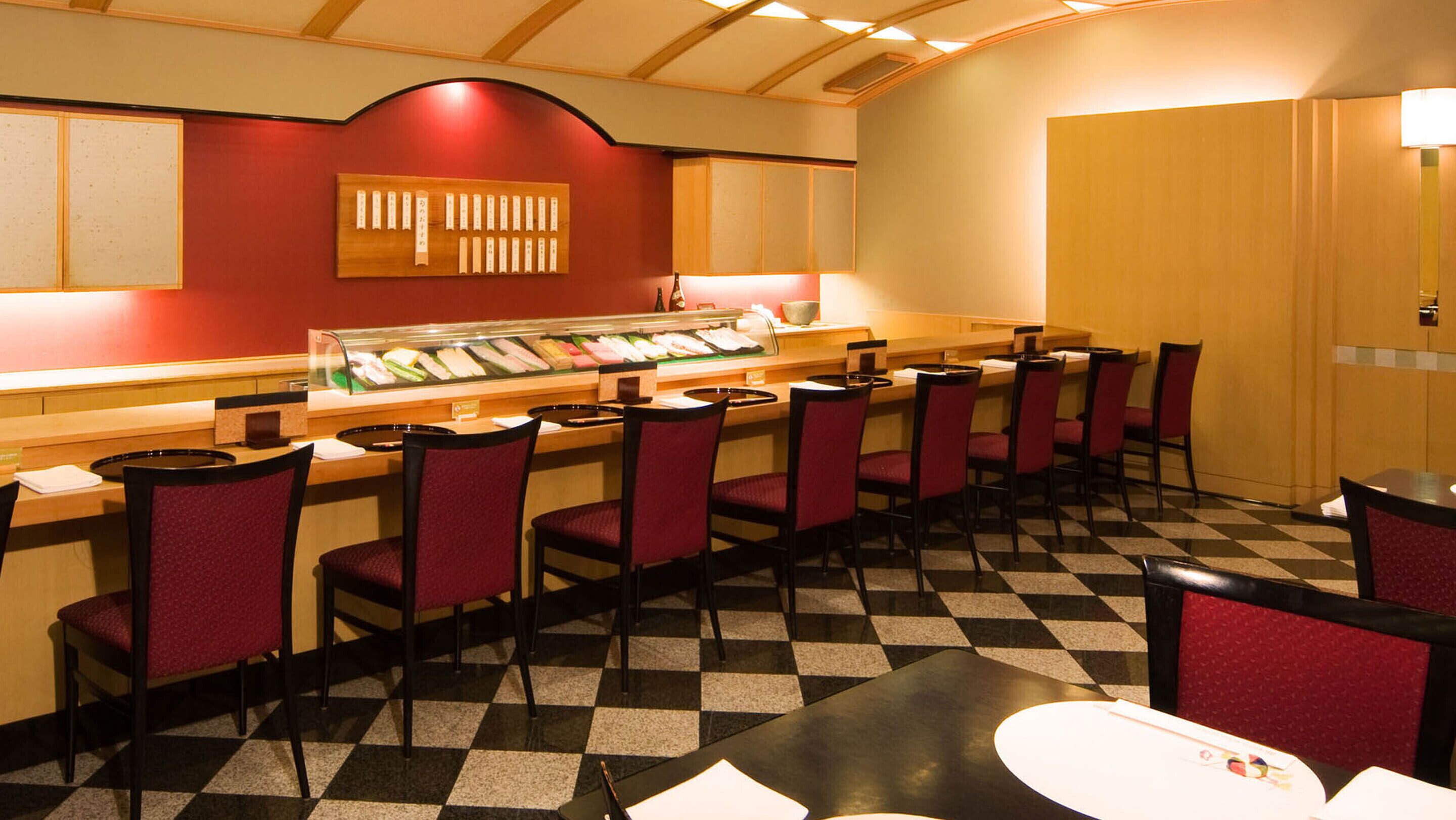 A restaurant with a checkered floor, red chairs, a sushi display, and wooden paneling.
