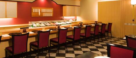 Un restaurant avec un sol à carreaux, des chaises rouges, un présentoir à sushis et des lambris en bois.