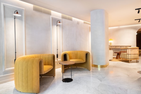 Un hall d’entrée moderne avec deux fauteuils jaunes, une table ronde et une grande colonne.