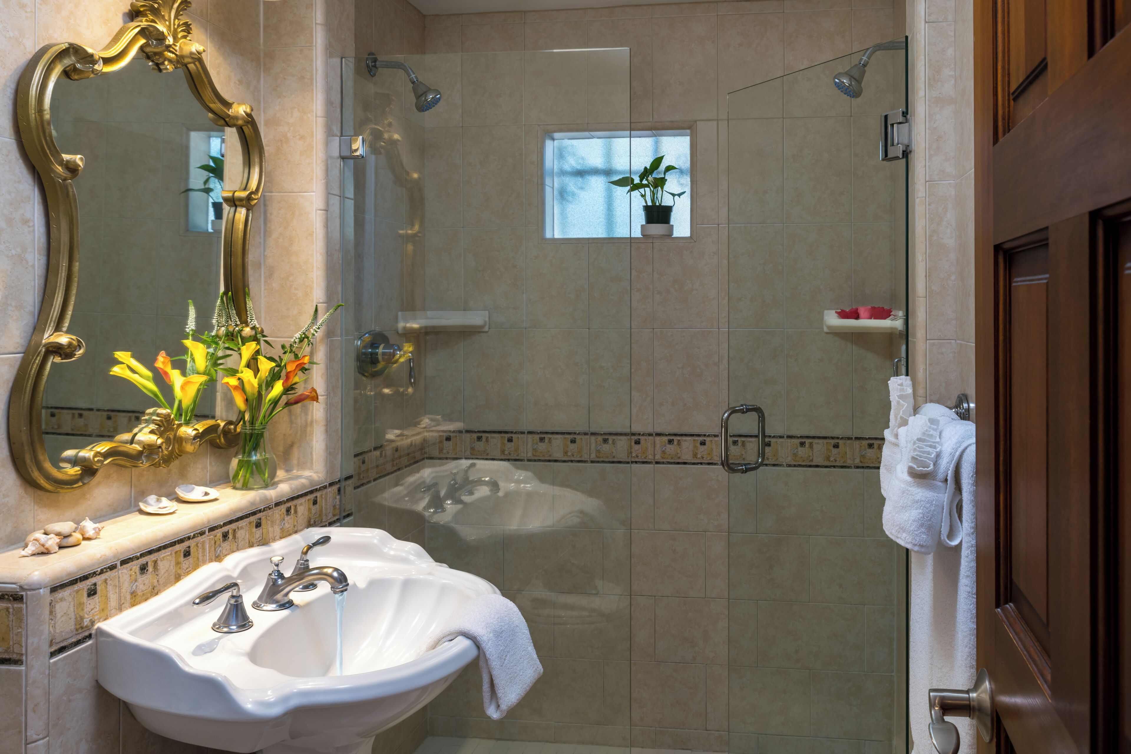 Une salle de bain avec un grand miroir, un lavabo, une douche et une plante en pot.