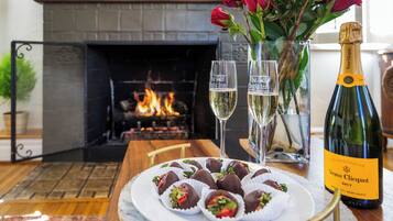 Une assiette de fraises enrobées de chocolat, deux coupes à champagne et une bouteille de Veuve Clicquot sur une table devant une cheminée.
