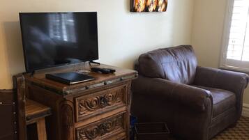 A living room with a television on a wooden dresser, a brown leather sofa, and a patterned carpet.