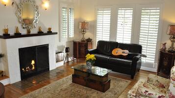 A living room with a fireplace, a black leather sofa, a glass coffee table, and a floral armchair.
