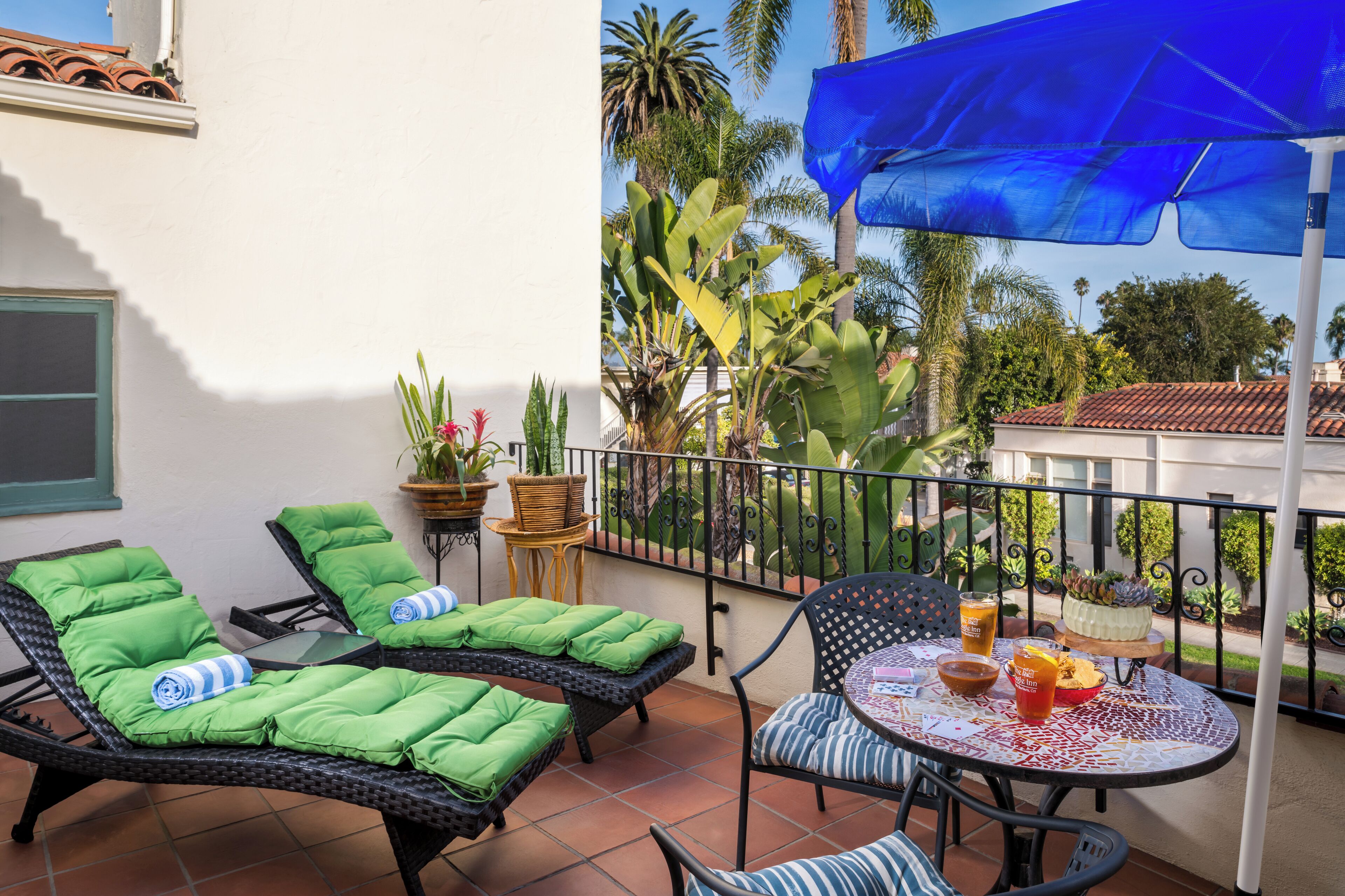 A balcony with two lounge chairs, a table with drinks, and potted plants.