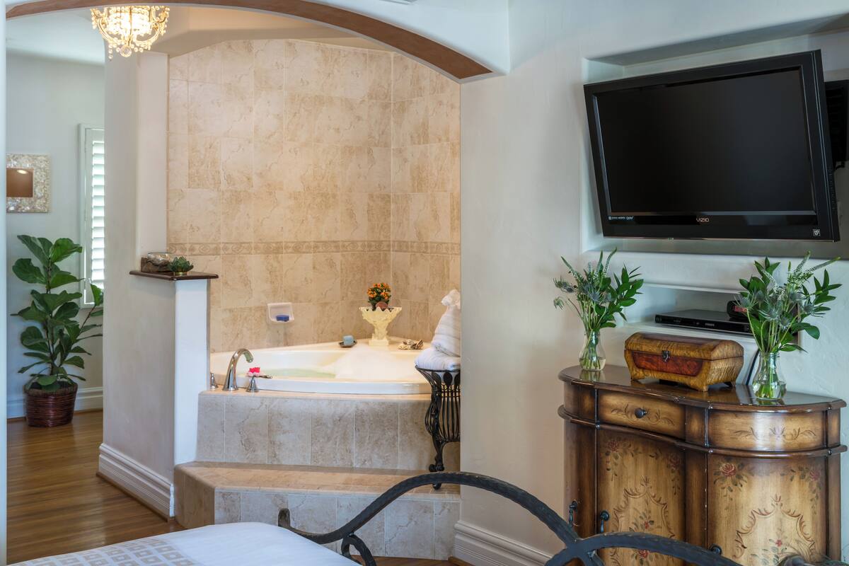 A bathroom with a bathtub, a television mounted on the wall, and a wooden cabinet with decorative items.