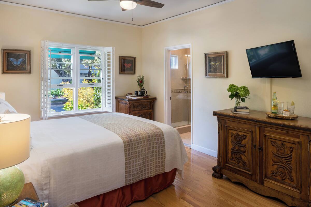 A bedroom with a bed, a dresser, a television, and a window with shutters.