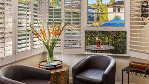 Ein Zimmer mit zwei Ledersesseln, einem kleinen Tisch mit Blumenvase und Blick auf einen Balkon mit Tisch und Stühlen.